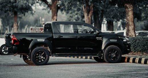 pexels-photo-18240251-18240251 Side view of a black Toyota Hilux pickup truck parked among trees.