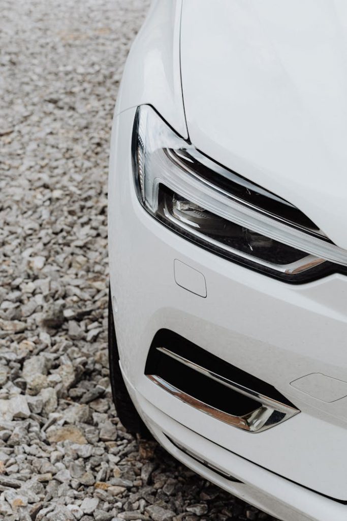 pexels-photo-4749996 Detailed view of a white car on gravel, focusing on headlights and design.